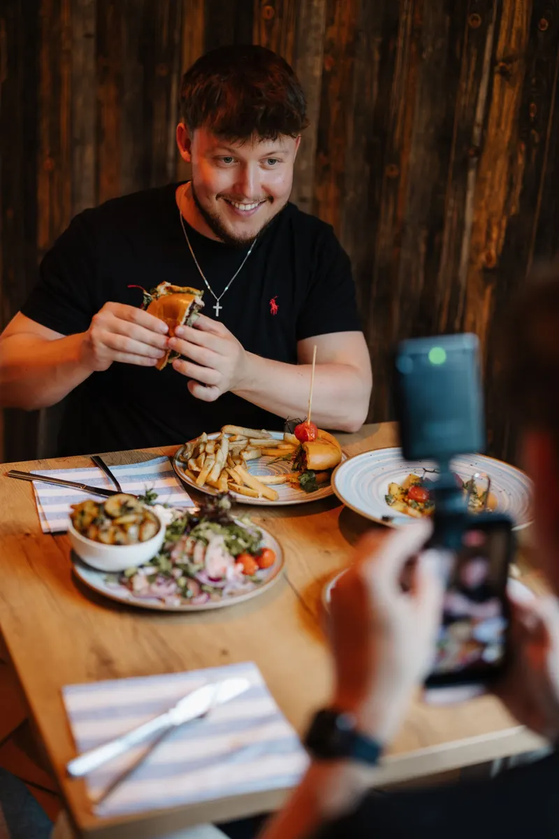 Mica beim Food-Dreh mit Burger, im Vordergrund das Smartphone mit Licht